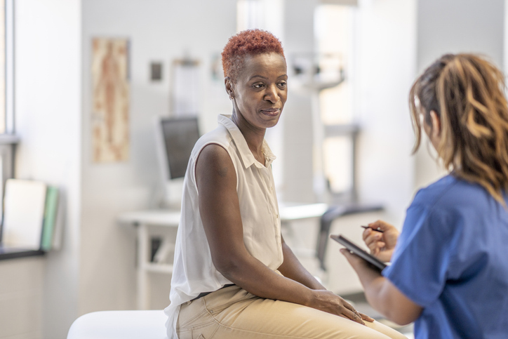 Black woman seated on exam table listening to her nurse speak