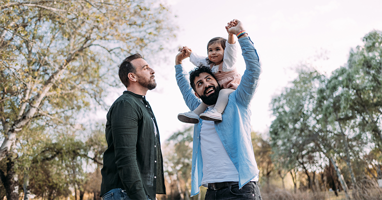 two gay parents with their child on one's shoulders