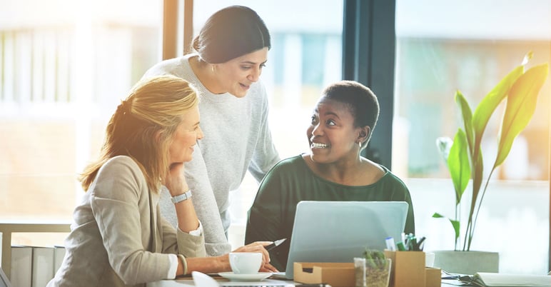 three women at work huddling over laptop