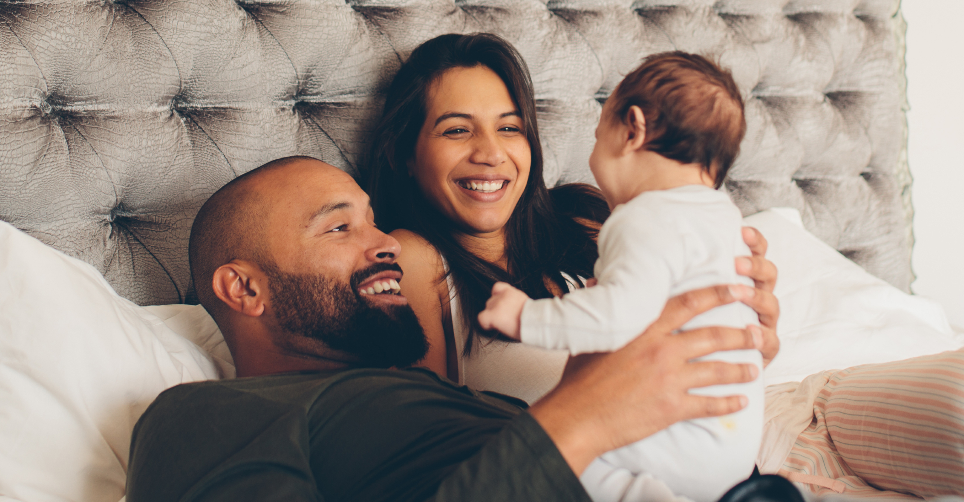 father and mother holding up their newborn while resting in bed