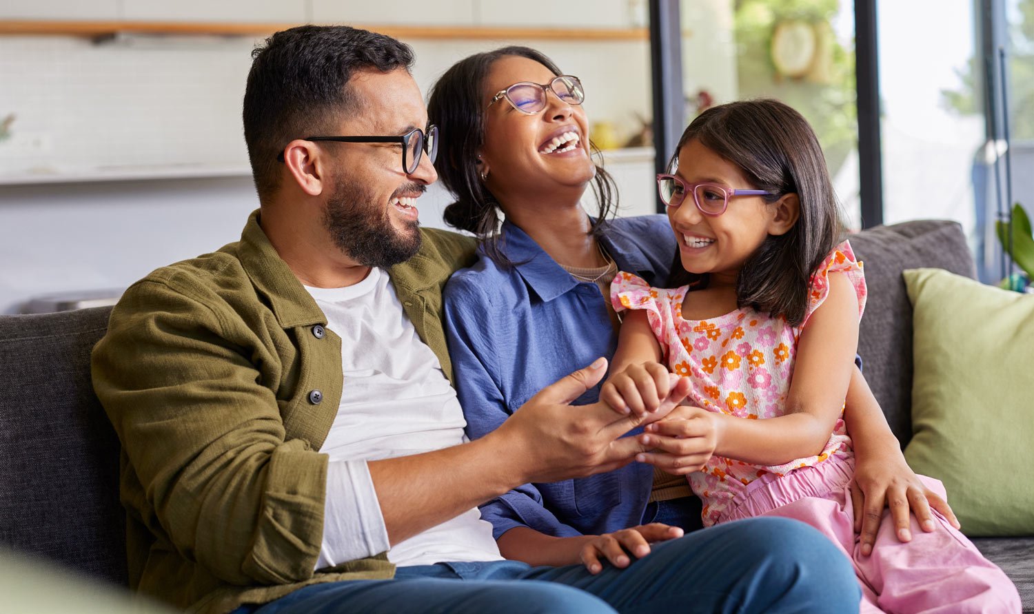 parents-laughing-with-their-daughter-on-the-couch-cropped