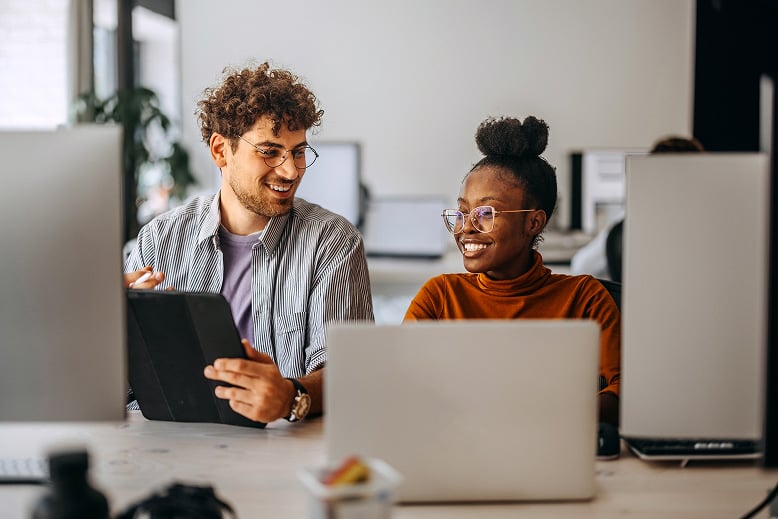 two-colleagues-at-work-chatting-in-front-of-their-laptops