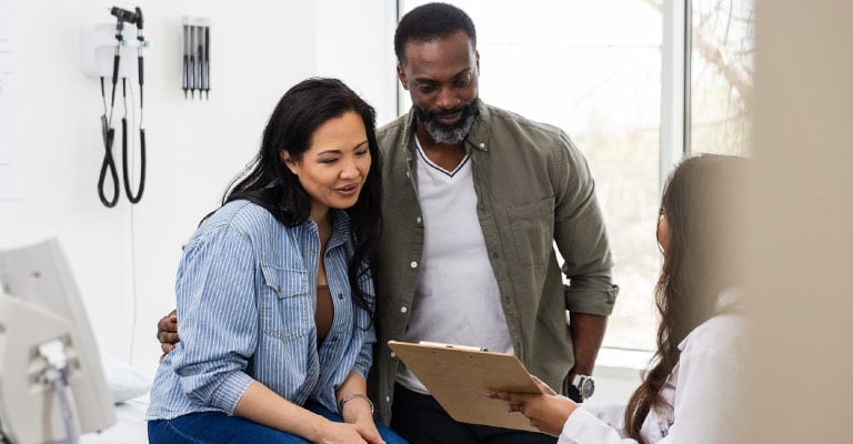 couple-at-doctors-office-smiling-at-clipboard