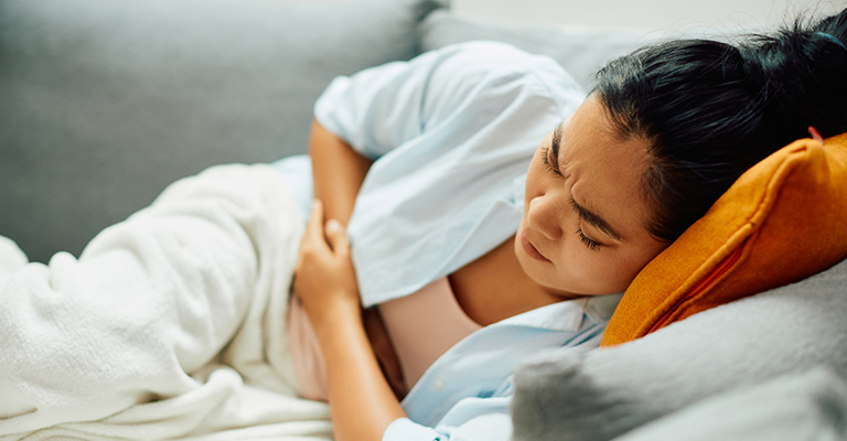 woman in pain laying on couch holding her stomach