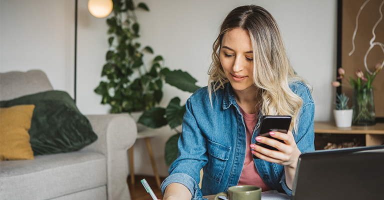 woman taking notes while researching on phone