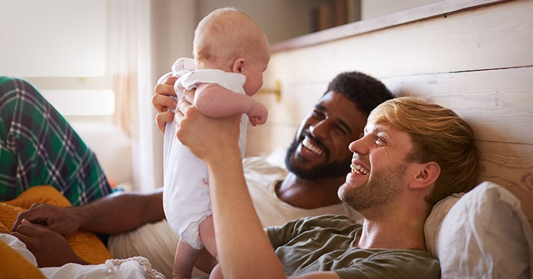 two gay men holding up their newborn
