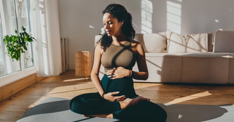 woman seated on a yoga mat, with hands on her stomach
