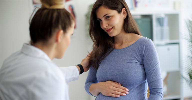pregnant woman resting her hand on her belly while smiling at provider