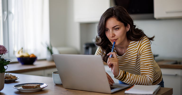 woman with pen looking at laptop