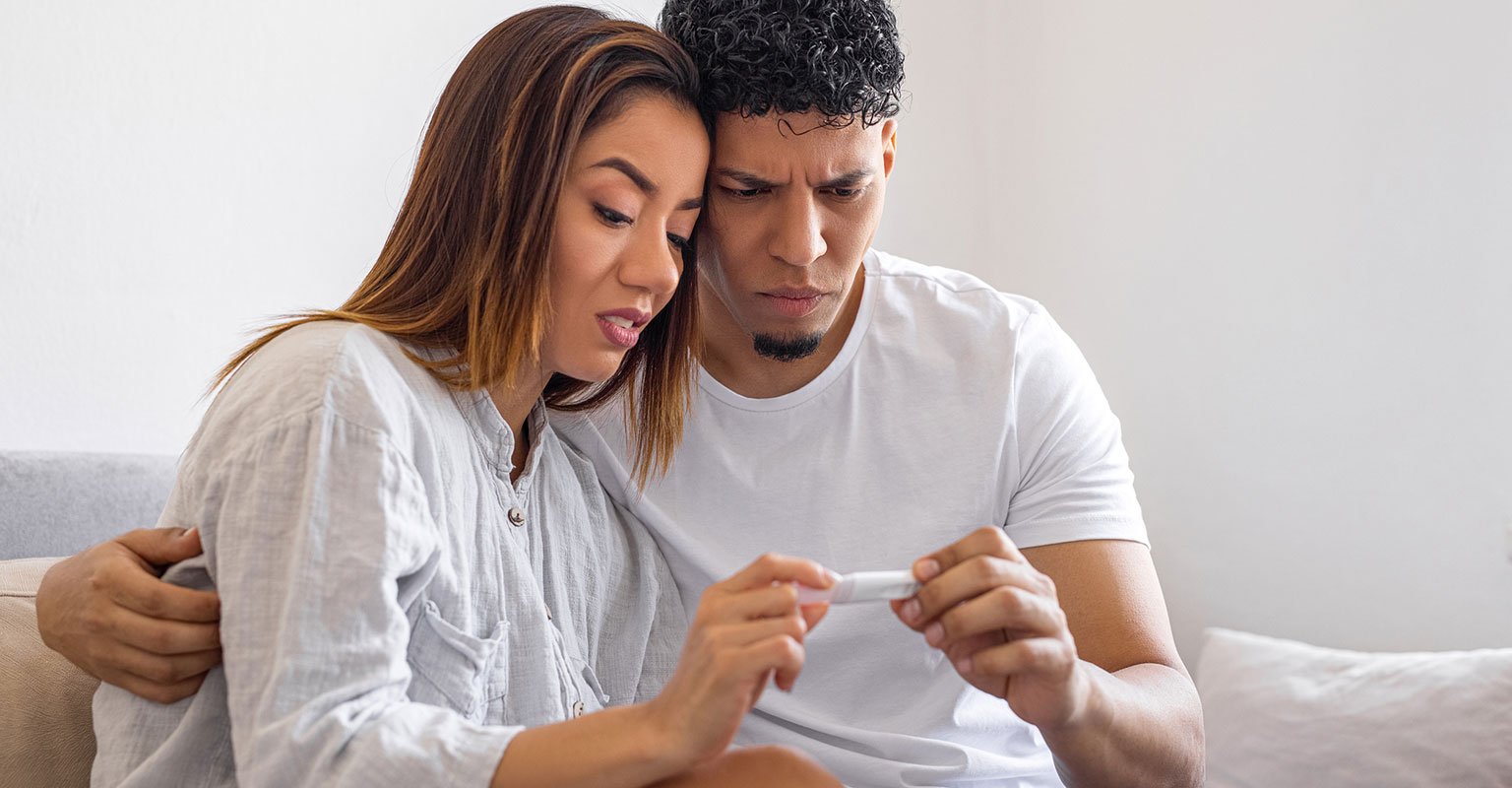 couple looking quizzically at a pregnancy test