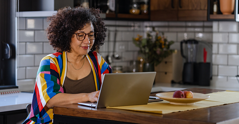 woman in midlife looking at laptop while seated at kitchen table