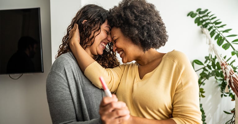 same-sex female couple embracing with a pregnancy test