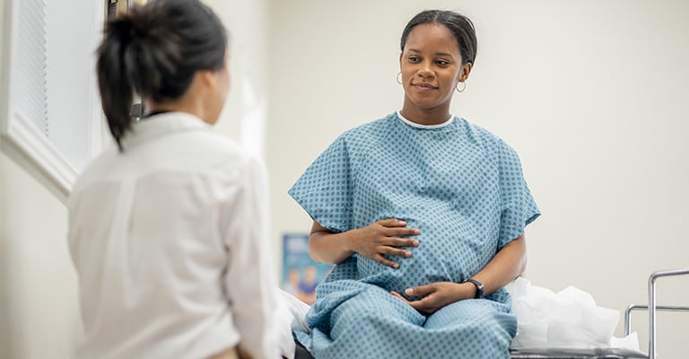 pregnant woman in hospital gown with provider in the exam room
