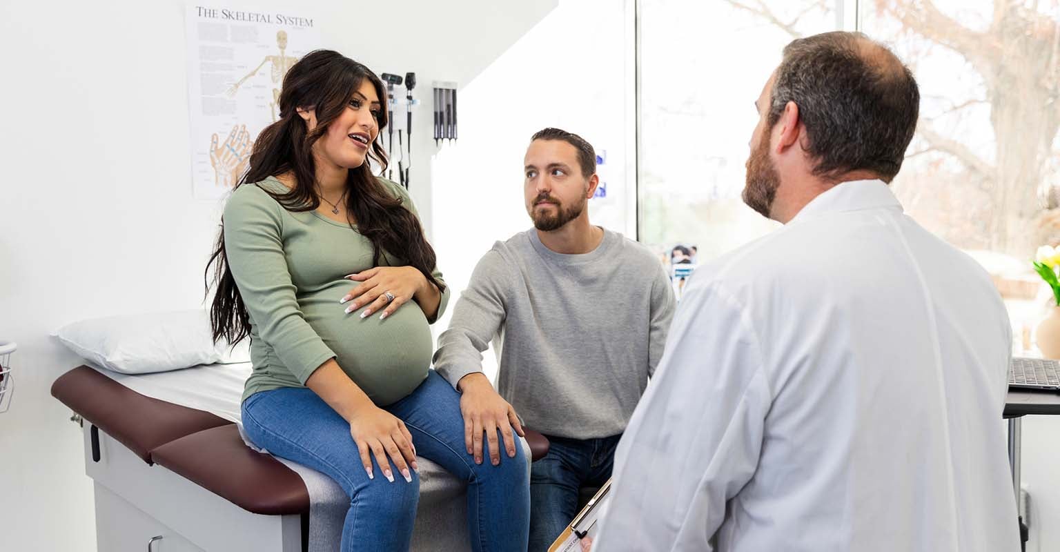 pregnant patient talking animatedly to her provider, with her partner looking on