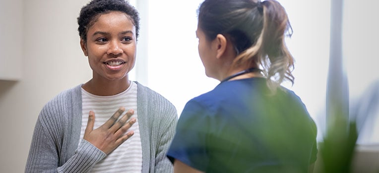 woman holding her hand over her heart while talking with provider