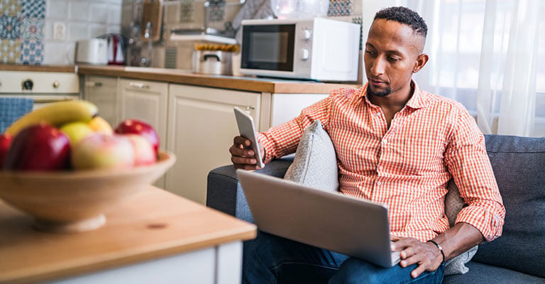 man in the kitchen looking at his phone and laptop