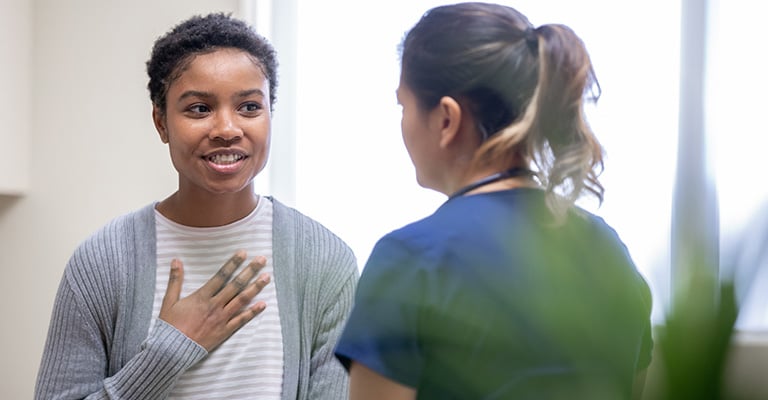 woman with her hand on her chest while talking to provider