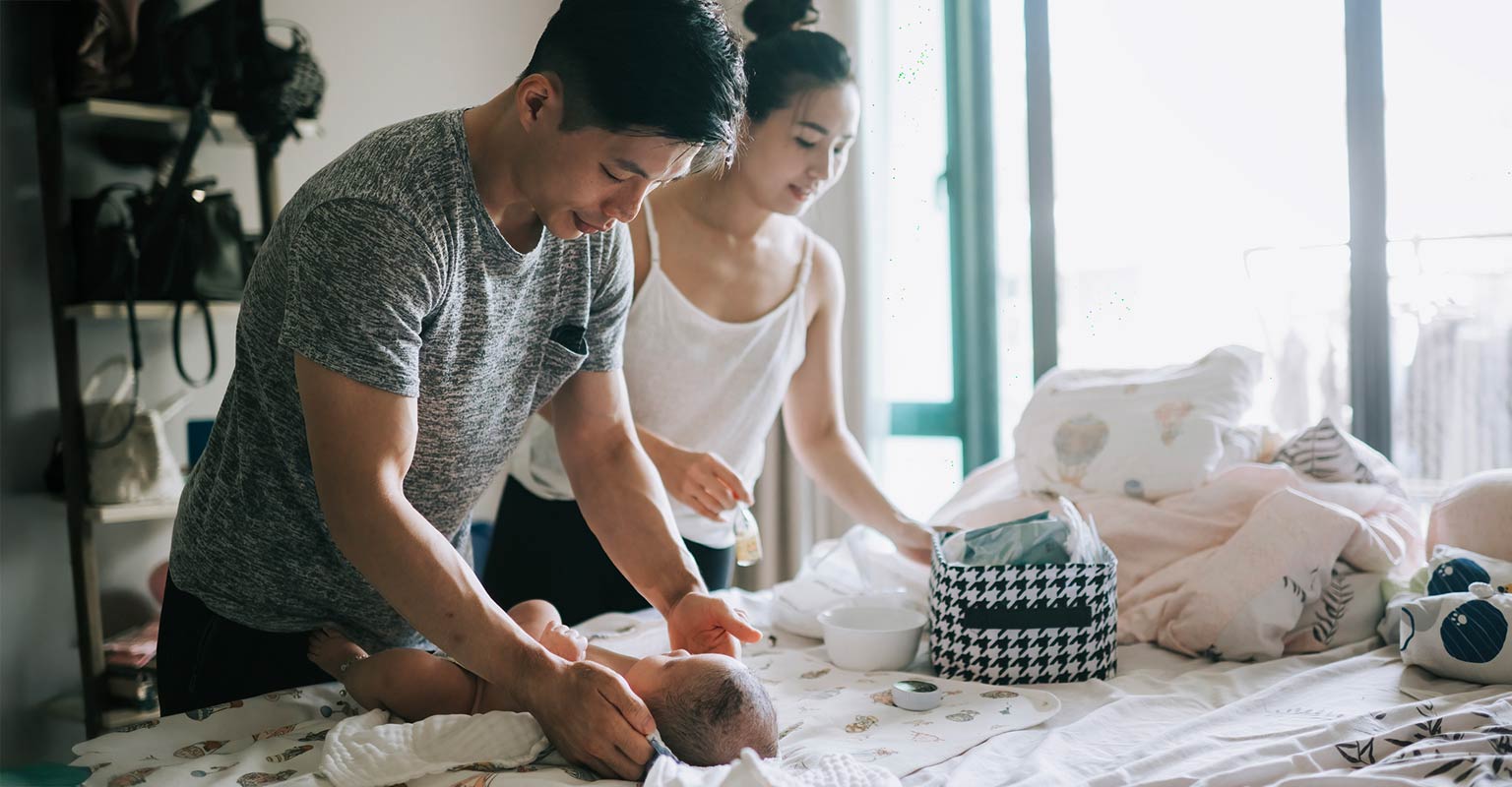 two parents helping to change a baby's diaper