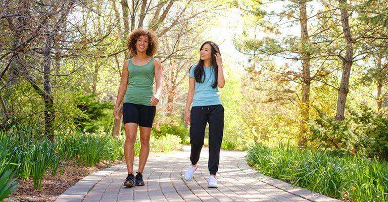 two friends in workout attire walking in the park