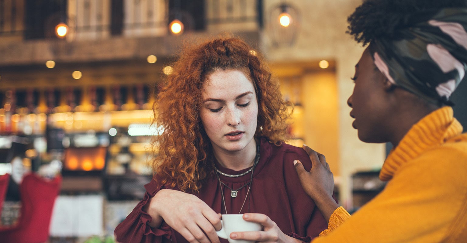woman with downcast eyes talking with a supportive friend