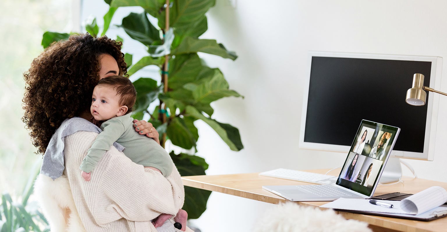woman cuddling newborn by her home office desk