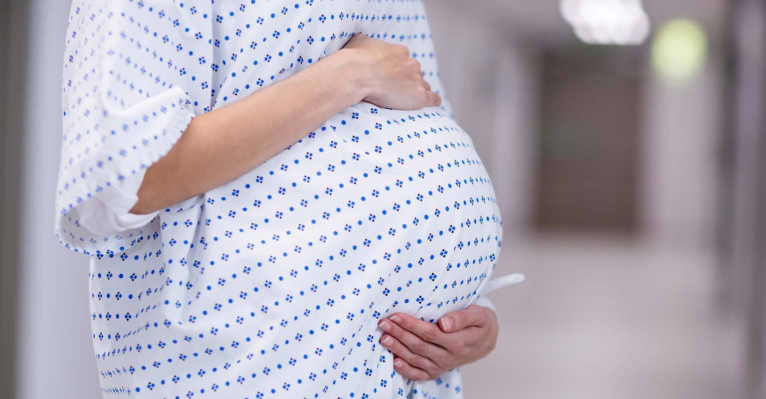 closeup of a pregnant woman cradling her belly wearing a hospital gown