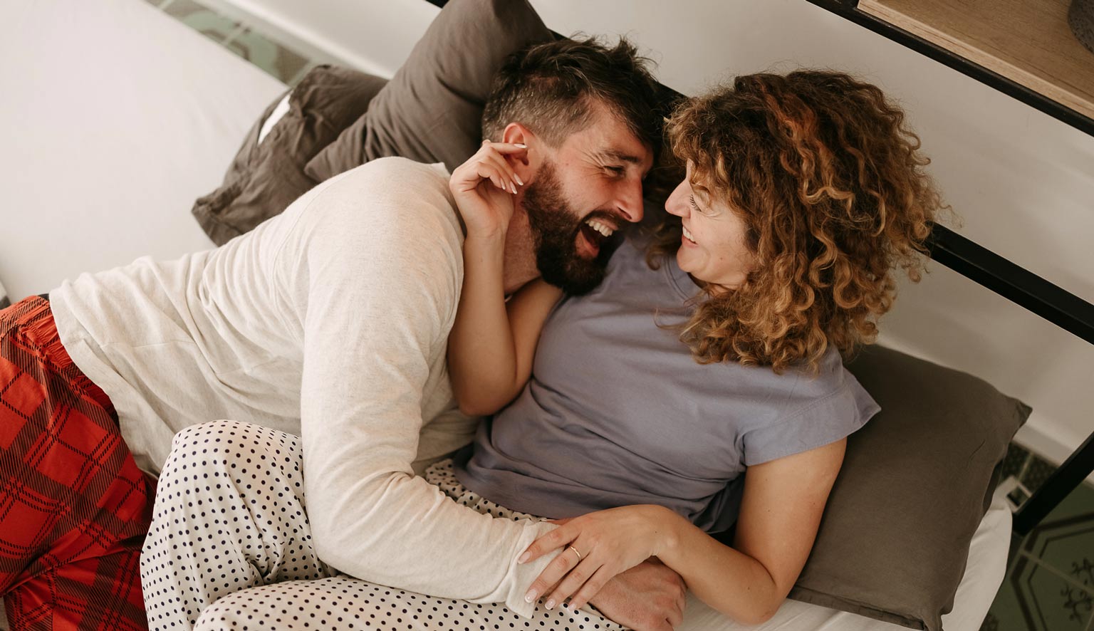couple lying in bed, laughing with each other in their pajamas