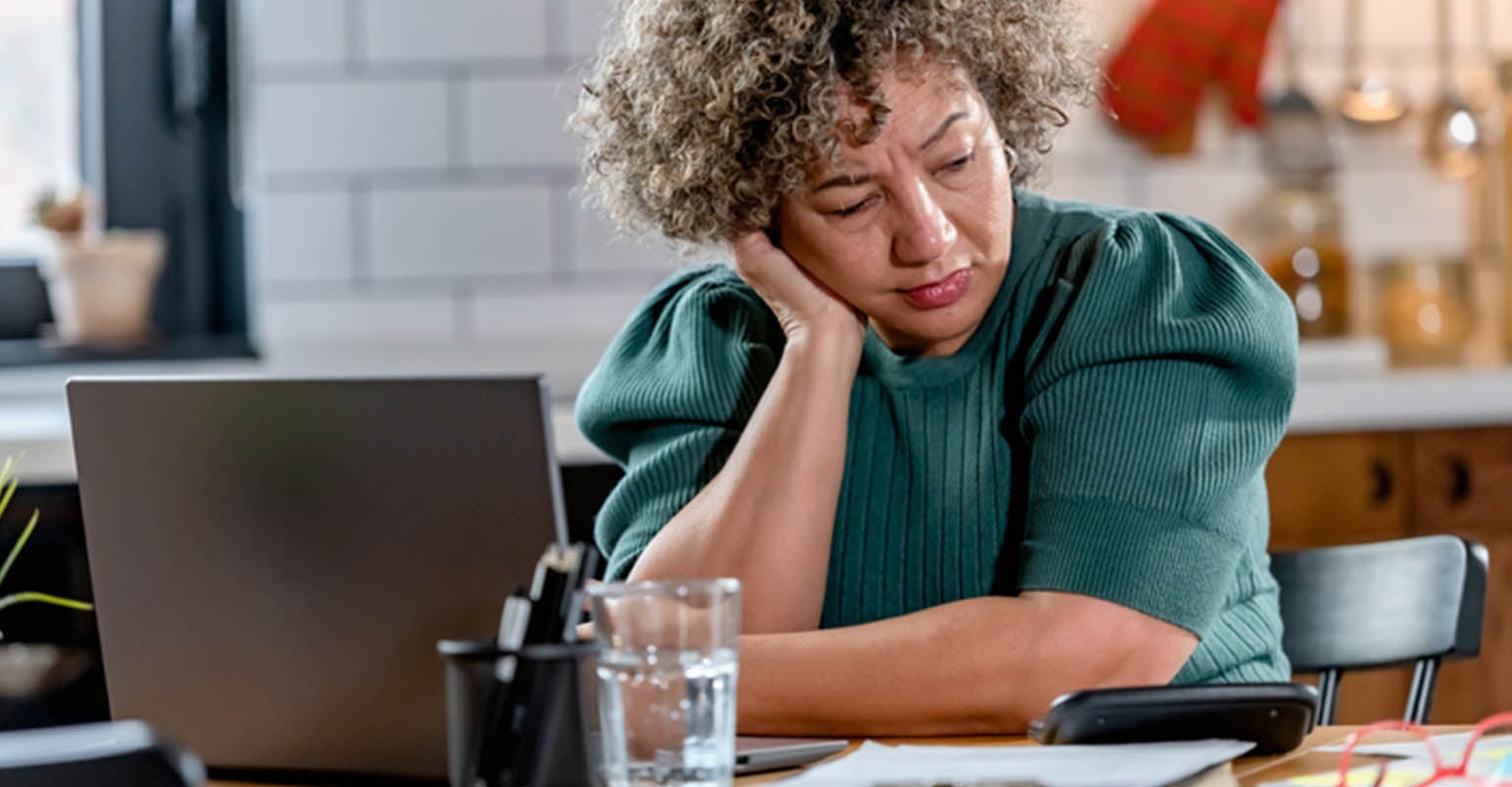 sleepy woman at her kitchen table by her laptop