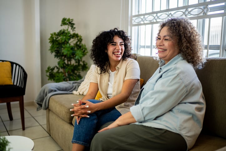 two friends seated on couch, happily conversing