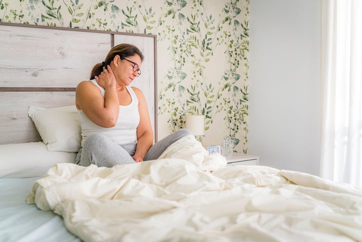 woman with neck pain seated in bed