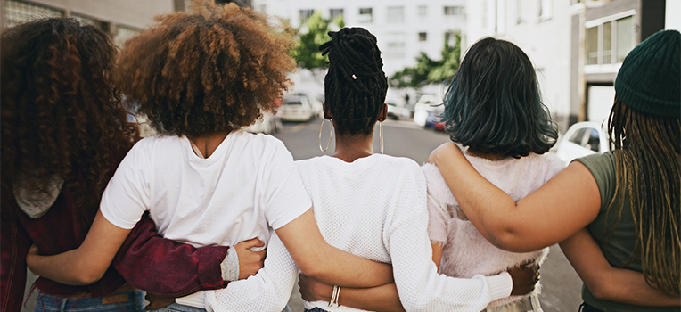 five Black women walking down the street with their arms around each other