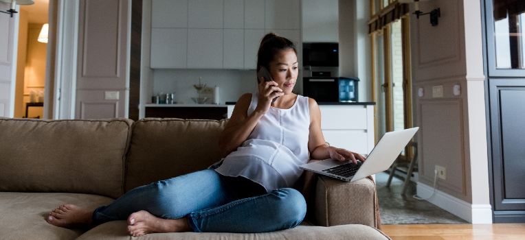 pregnant woman on sofa, looking at the computer and talking on the phone