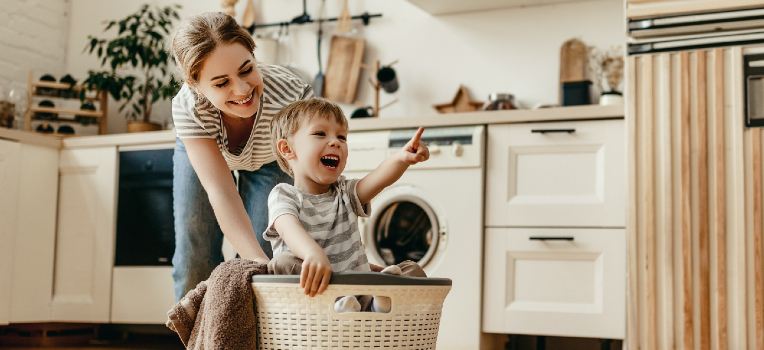 happy toddler in laundry basket pushed by mom