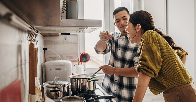 a wife trying her husband's cooking in the kitchen
