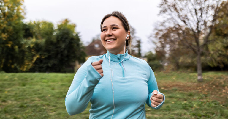 Woman jogging through a park listening to headphones