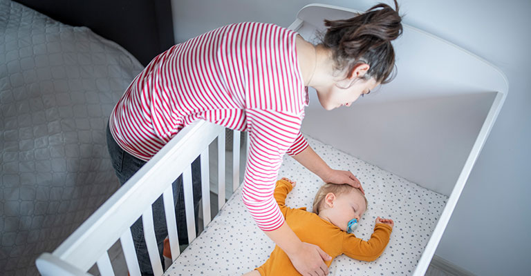 mother putting baby to sleep in a crib