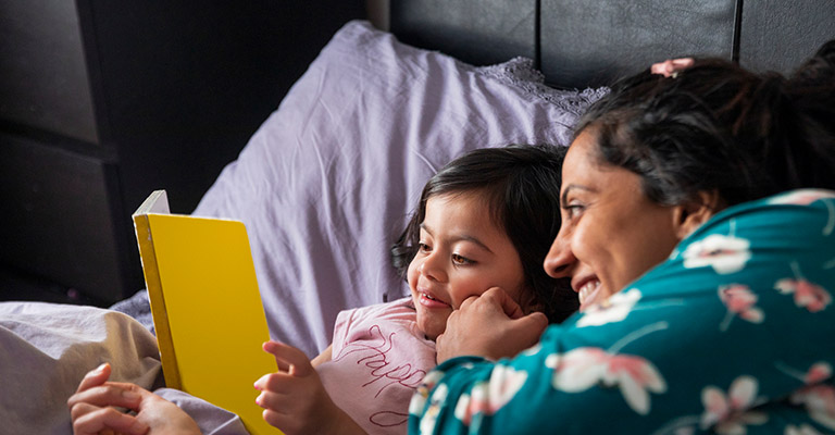 mother and daughter reading book before bedtime