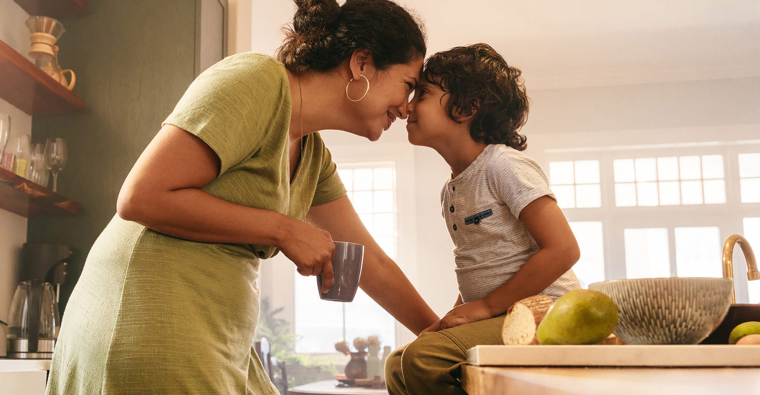 smiling mother and child with foreheads touching, with the child perched on the counter