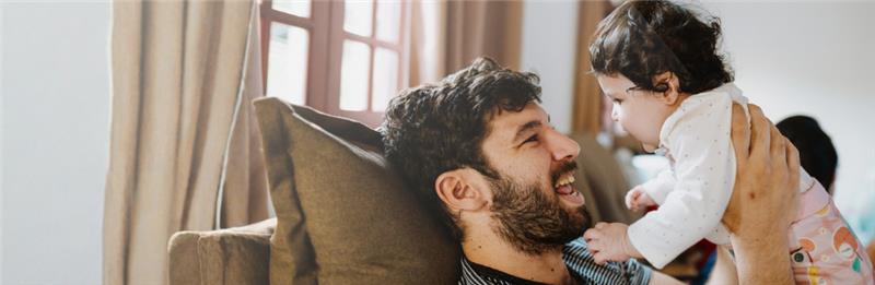 father happily holding baby on couch