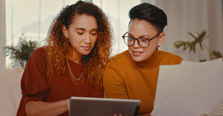 two women looking at tablet and paperwork on the couch
