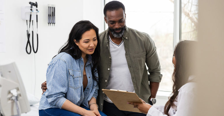couple at doctor's office smiling at results on a clipboard