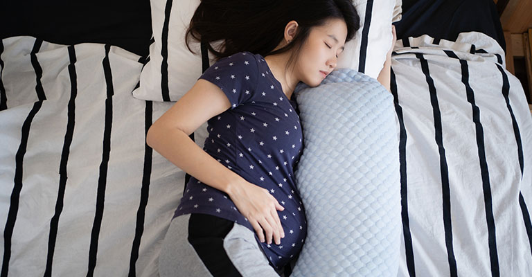 pregnant woman lying down on her side with pregnancy pillow