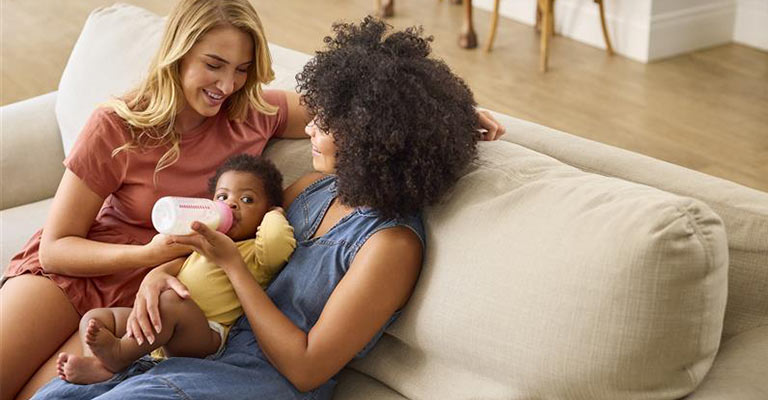 two women with baby, one feeding the baby with bottle