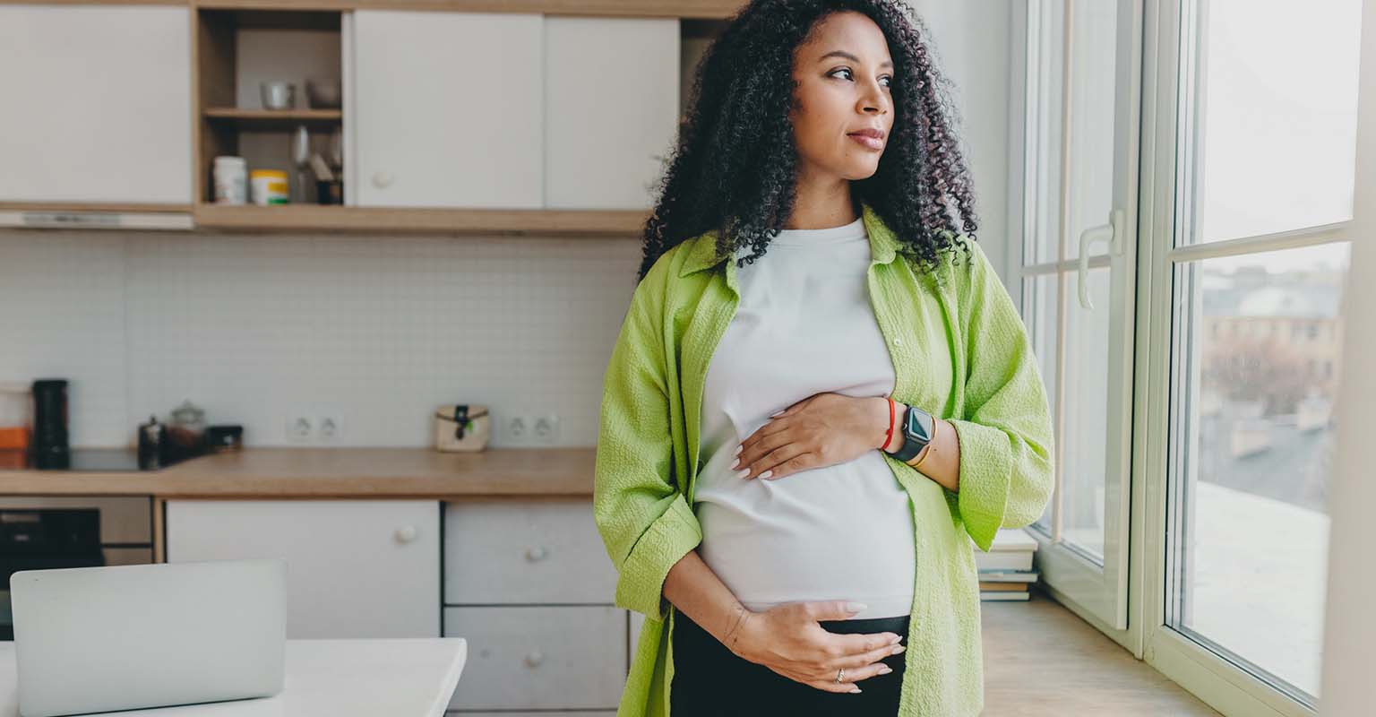pregnant woman looking out the window, cradling her belly