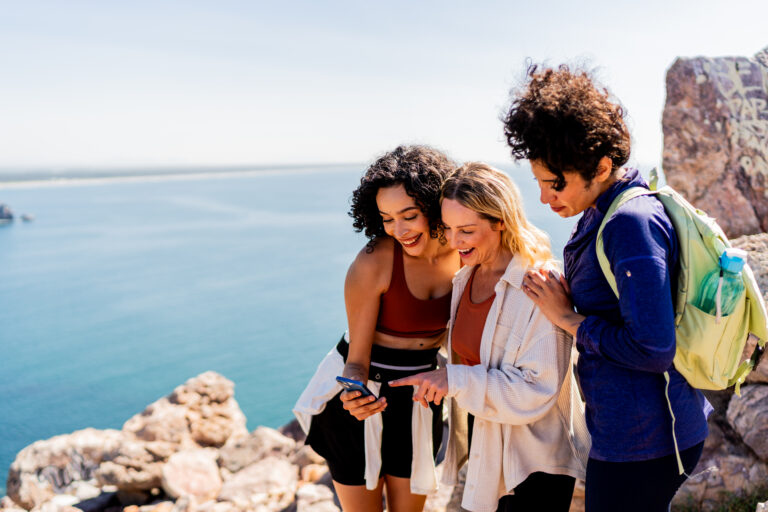 Friends women talking and using mobile phone during hiking on mountain peak